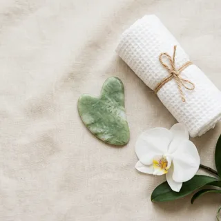 Jade gua sha stone with a rolled towel and orchid